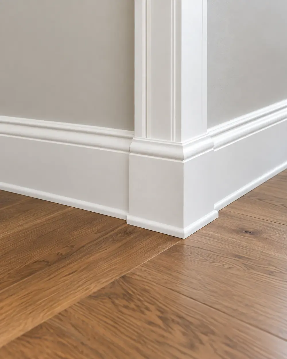 Baseboards and trim installation in Los Angeles: white baseboard and door casing meeting an oak floor