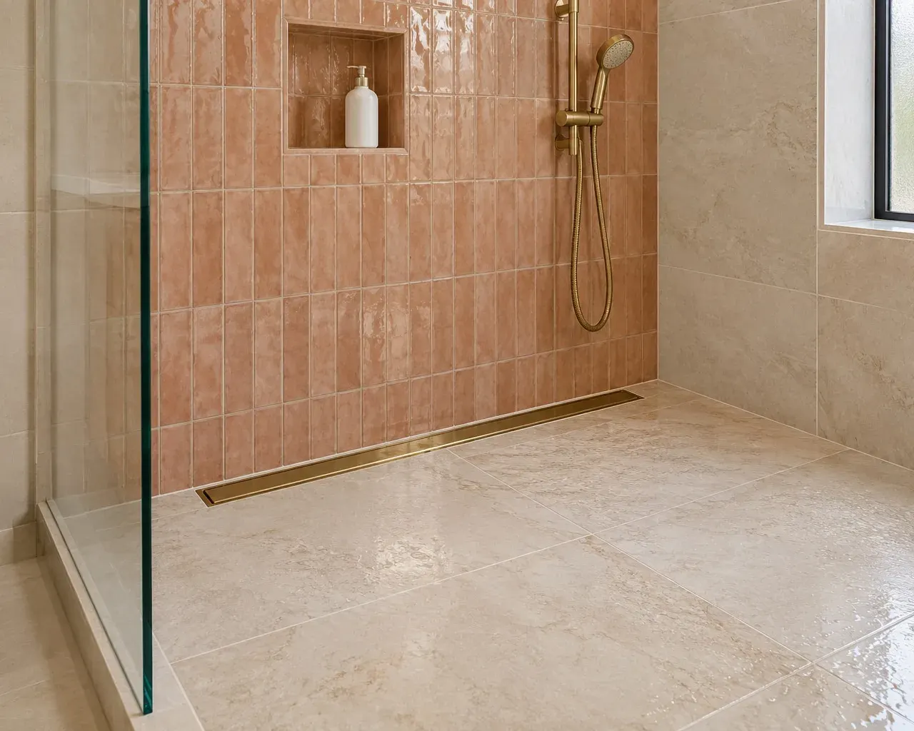 Shower floor detail with a linear drain, large limestone-look floor tile and a handheld shower on a slide rail in a Southern California bathroom