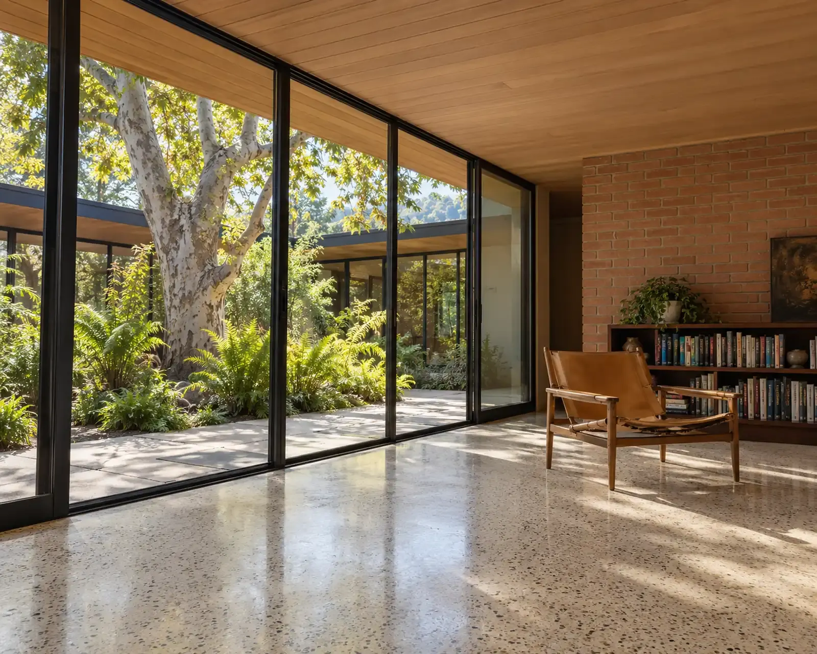 Living room with floor-to-ceiling black-framed sliding glass doors opening to a garden courtyard, polished concrete floor and brick wall