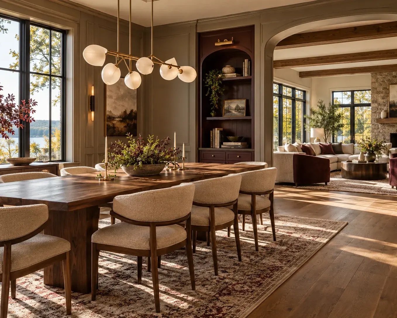 Dining room with a wood table, upholstered chairs, wide-plank oak floors and large black-framed windows, open to a living room with a fireplace
