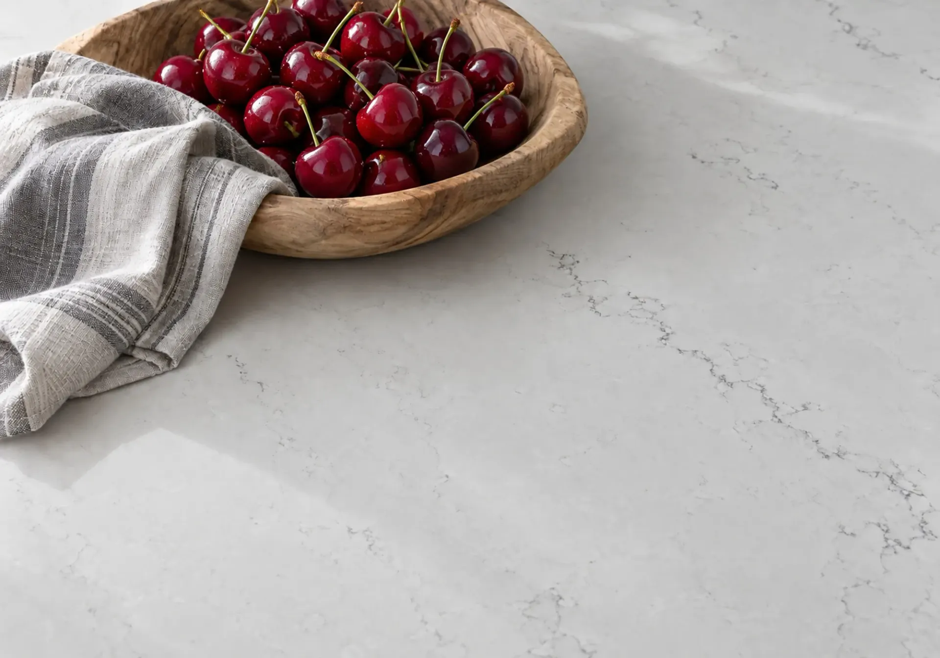 Quartz countertops in Los Angeles, CA: light gray quartz surface with subtle veining, a wooden bowl of cherries and a striped linen towel